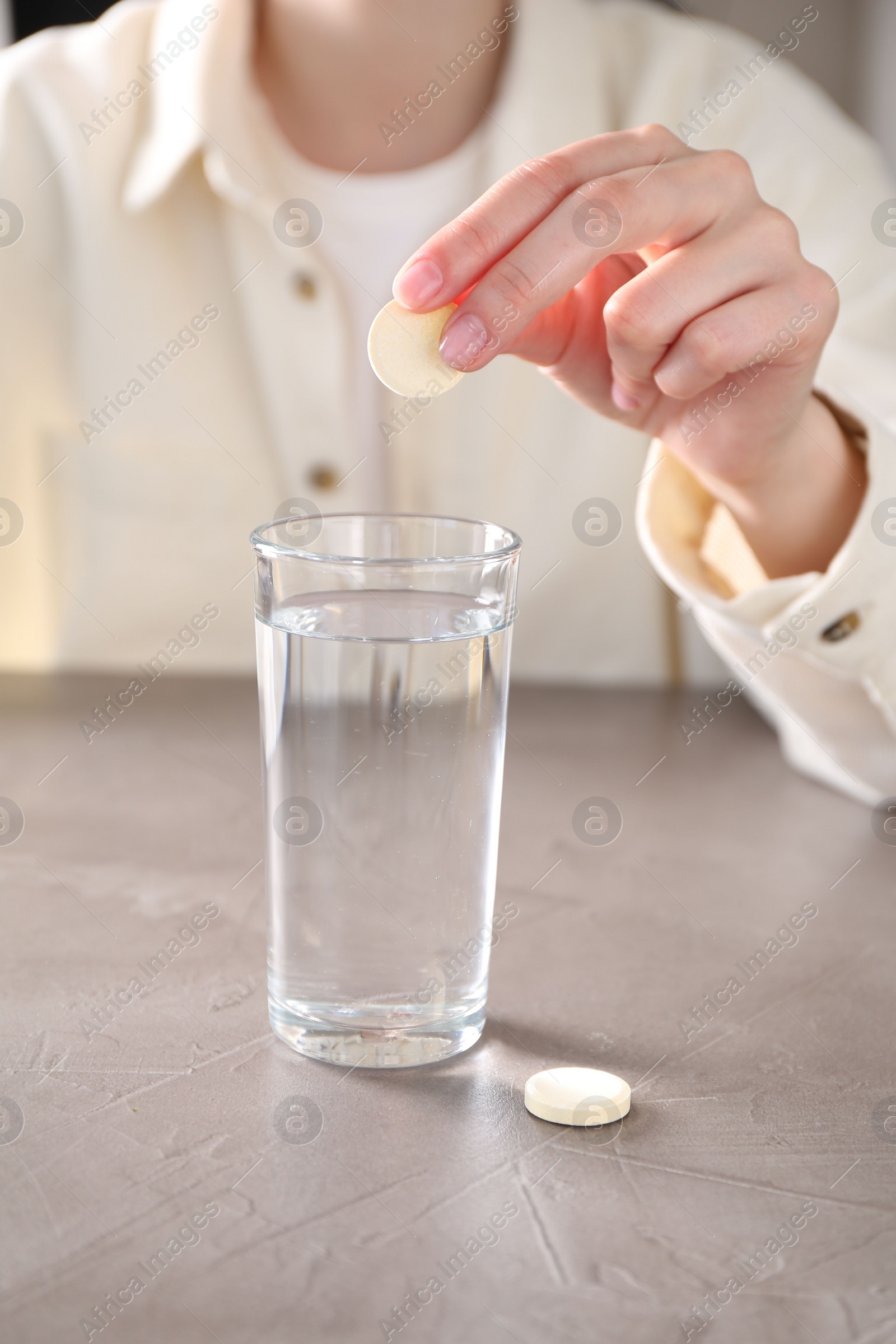 Photo of Woman putting effervescent pill into glass of water at grey table, closeup