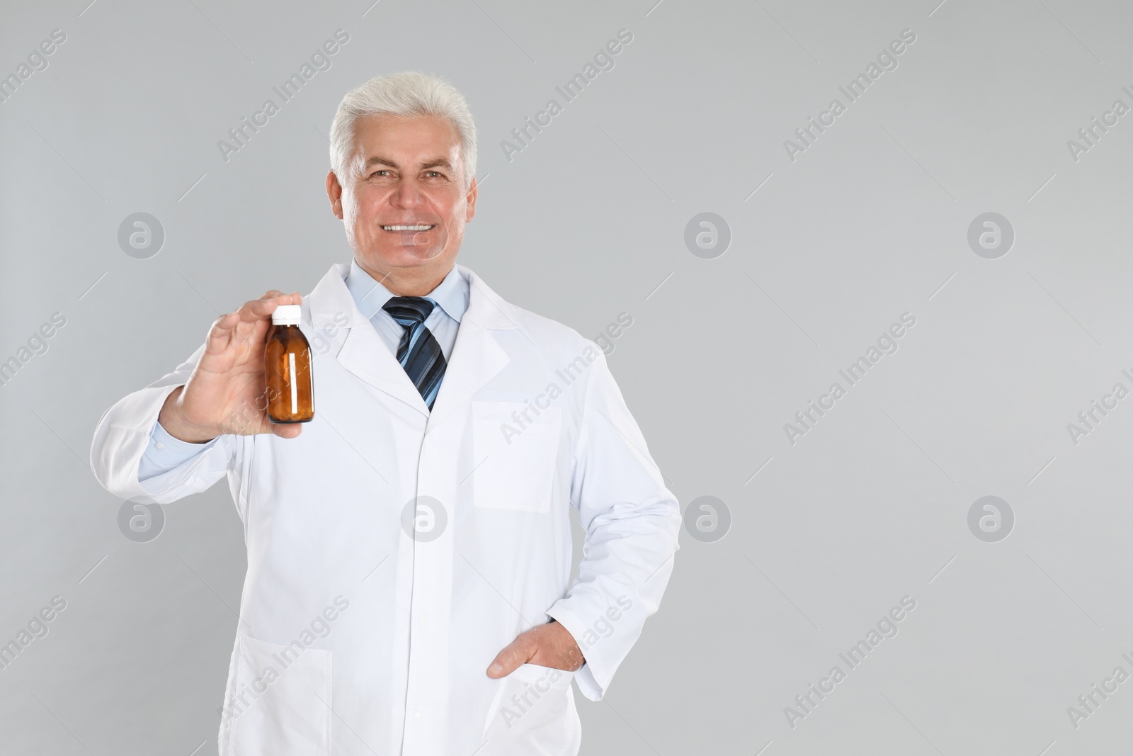 Photo of Senior pharmacist with syrup on light grey background. Space for text