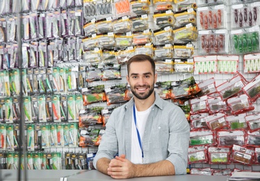 Photo of Salesman standing near showcase with fishing equipment in sports shop