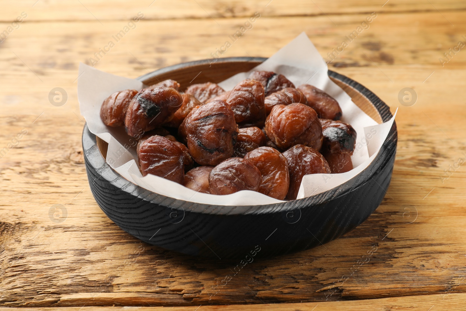 Photo of Roasted edible sweet chestnuts in bowl on wooden table