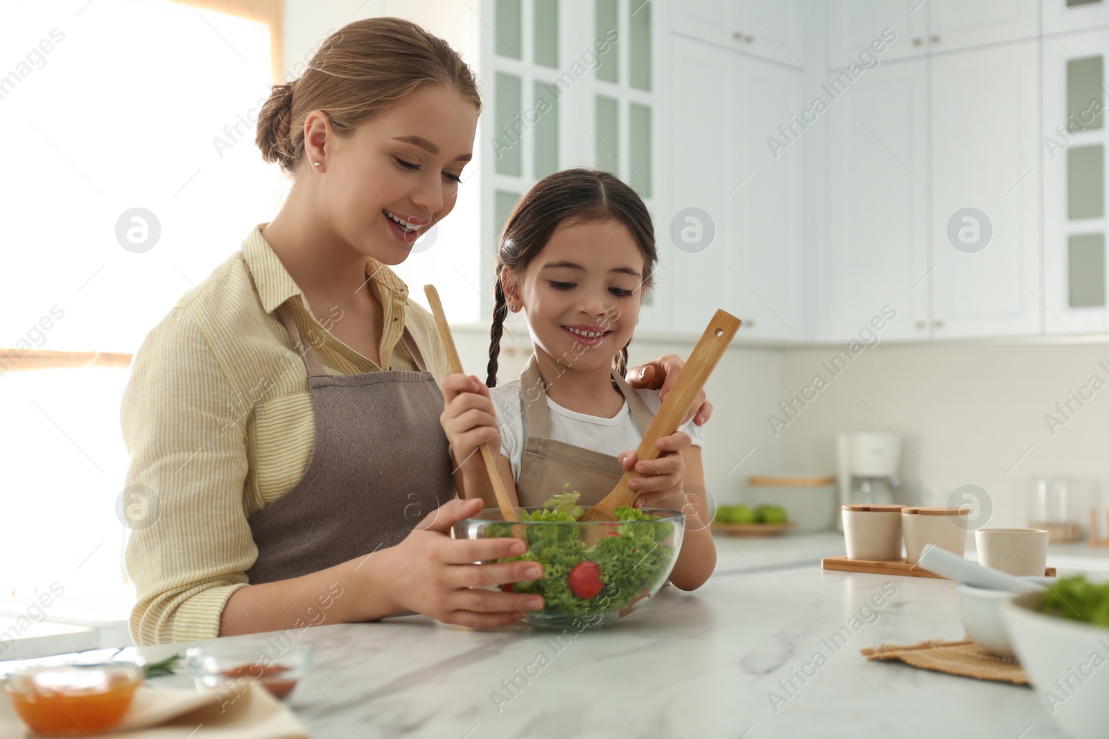 Photo of Mother and daughter cooking salad together in kitchen