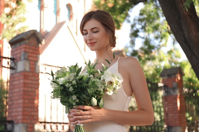 Photo of Gorgeous bride in beautiful wedding dress with bouquet near church