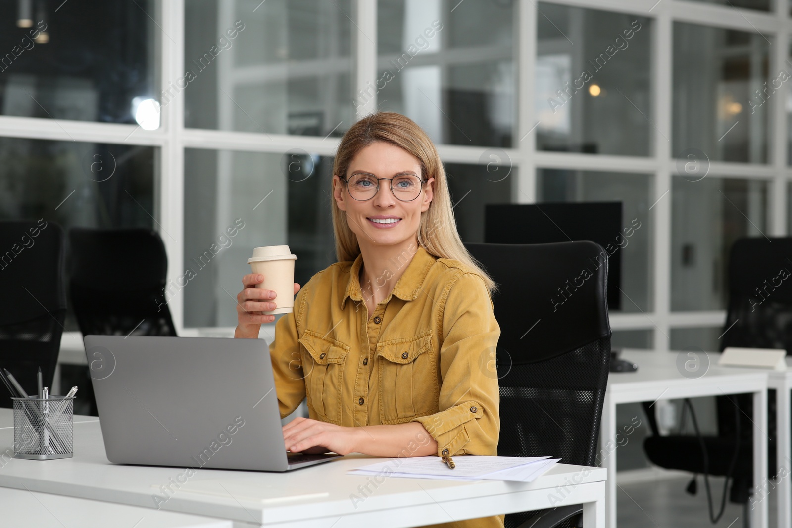 Photo of Woman with cup of coffee working on laptop at white desk in office