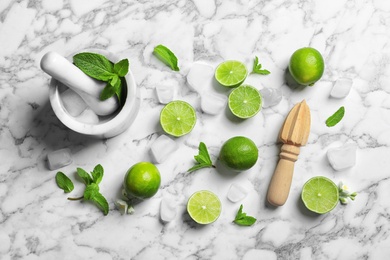 Flat lay composition with lime, juicer and mortar on marble background. Refreshing beverage ingredients