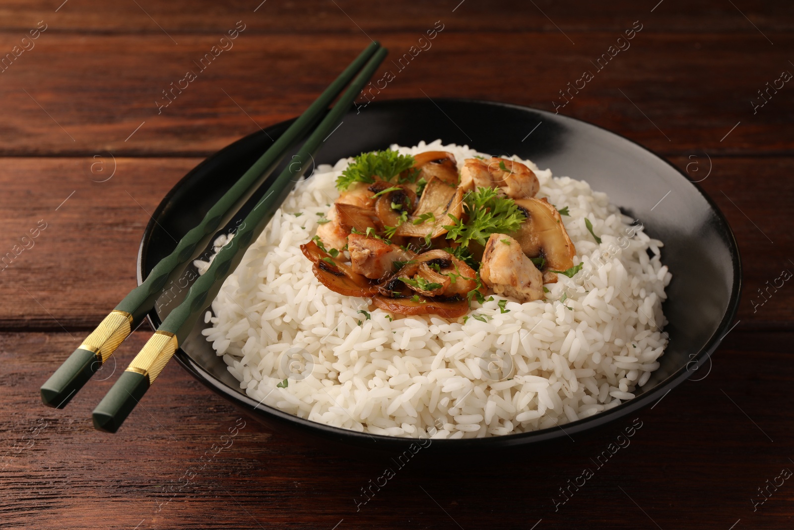 Photo of Delicious rice with mushrooms, parsley and chopsticks on wooden table, closeup