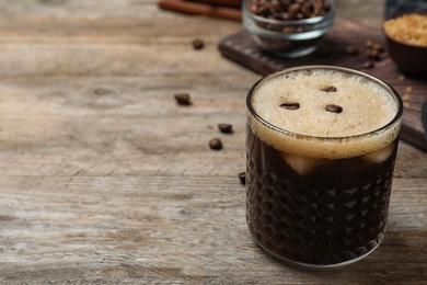 Glass of delicious coffee cocktail on wooden table. Space for text