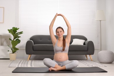 Pregnant woman doing exercises on yoga mat at home