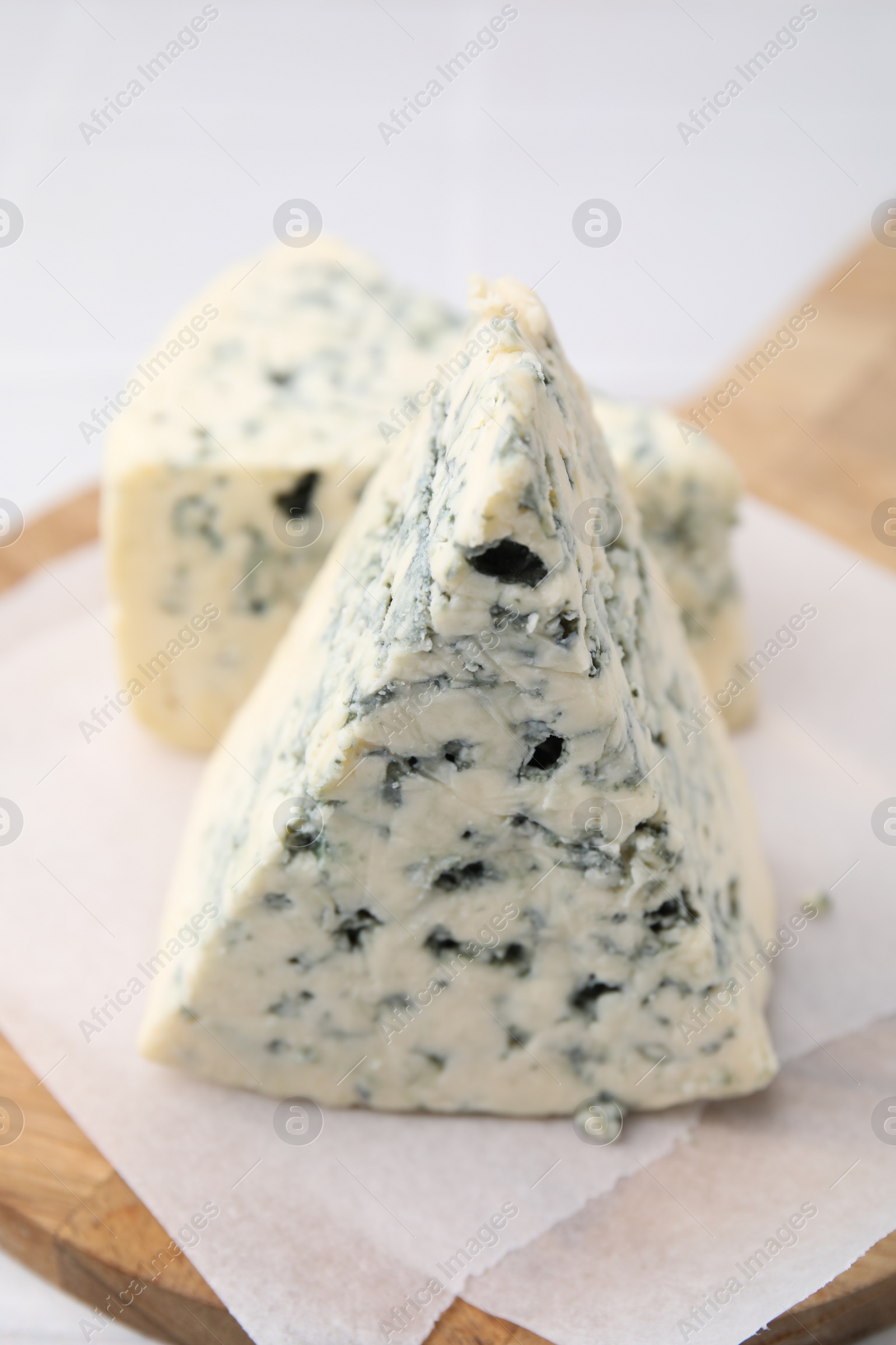 Photo of Wooden cutting board with blue cheese on white tiled table