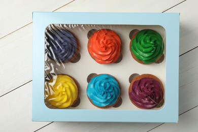Box with different cupcakes on white wooden table, top view