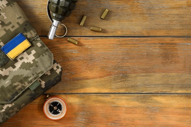 Photo of Tactical gear, military uniform and Ukrainian army patch on wooden table, flat lay. Space for text
