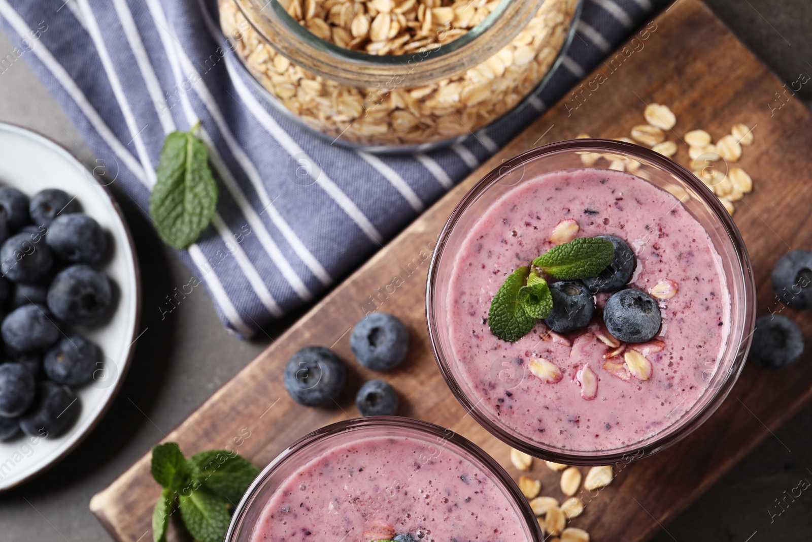 Photo of Glasses of tasty blueberry smoothie with oatmeal on dark grey table, flat lay
