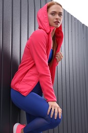 Beautiful woman in gym clothes posing near dark grey fence on street