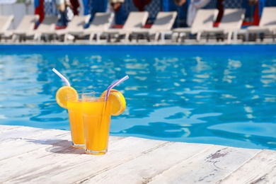 Photo of Refreshing cocktails near outdoor swimming pool on sunny day. Space for text