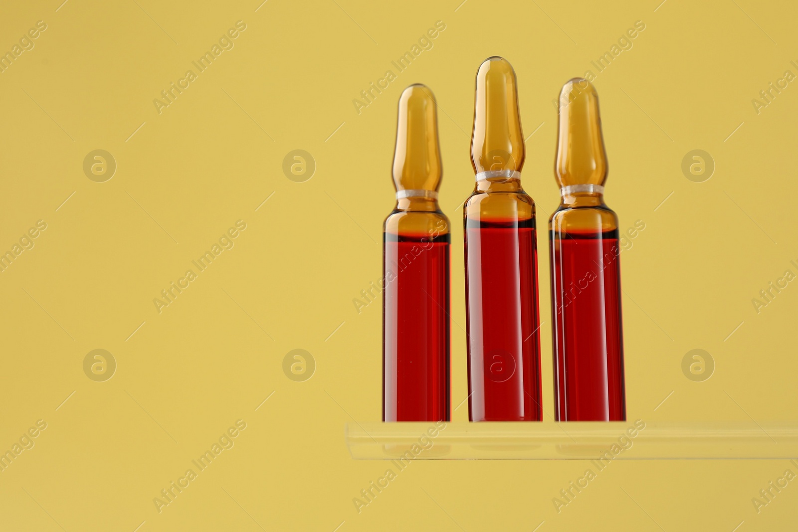 Photo of Glass ampoules with liquid on yellow background. Space for text