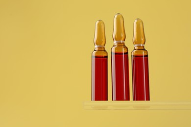 Glass ampoules with liquid on yellow background. Space for text