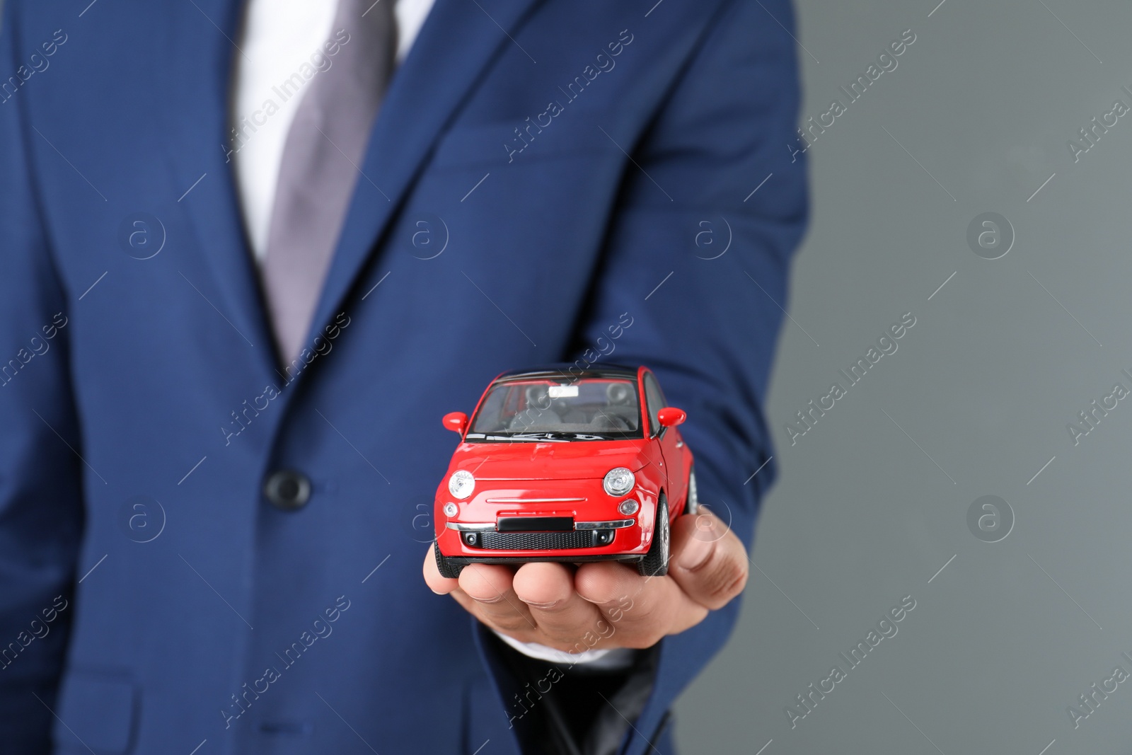 Photo of Insurance agent holding toy car on gray background, closeup