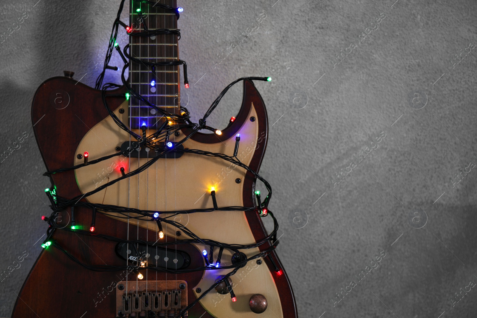 Photo of Guitar with colorful lights on grey stone background, space for text. Christmas music