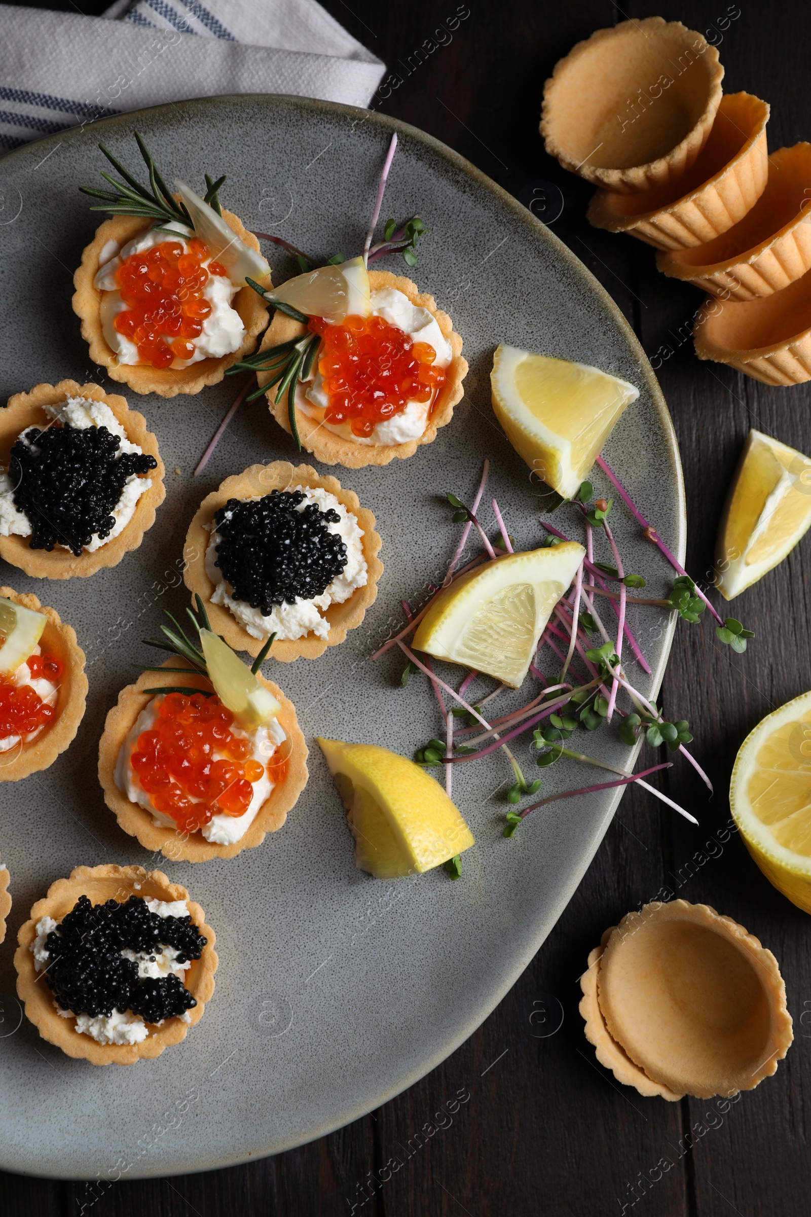 Photo of Delicious tartlets with red and black caviar served on wooden table, flat lay