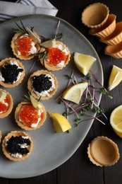 Delicious tartlets with red and black caviar served on wooden table, flat lay