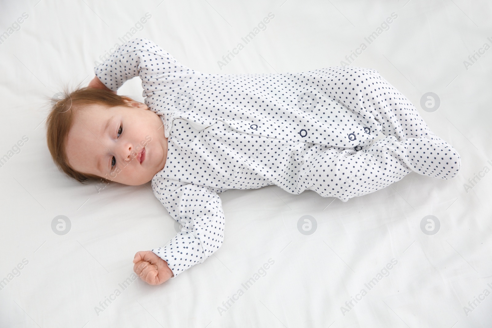 Photo of Adorable baby in cute footie on white sheet, above view
