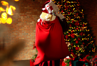 Photo of Santa Claus holding bag full of Christmas gifts in room