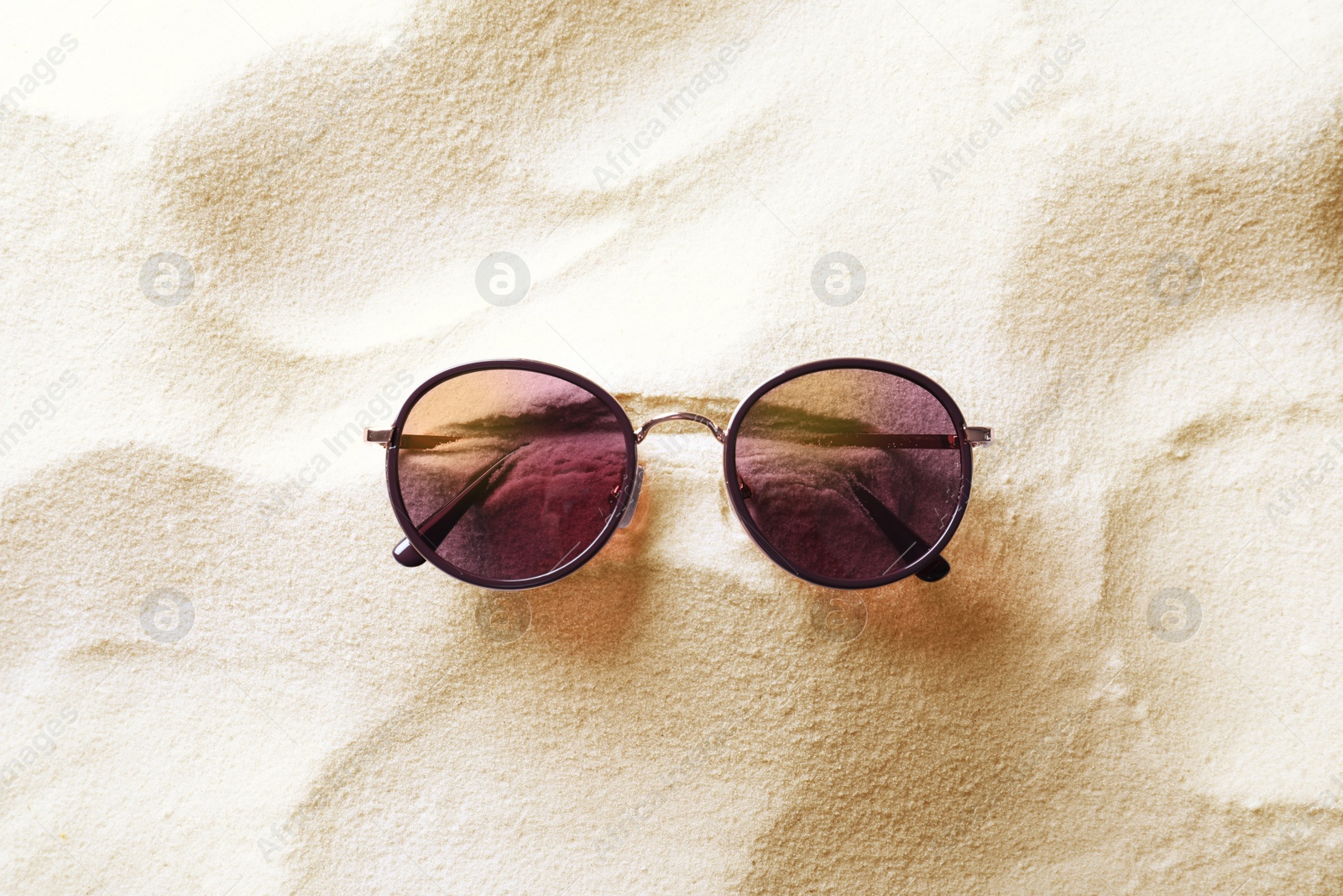 Photo of Stylish sunglasses on white sand, top view