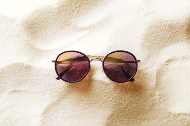 Stylish sunglasses on white sand, top view