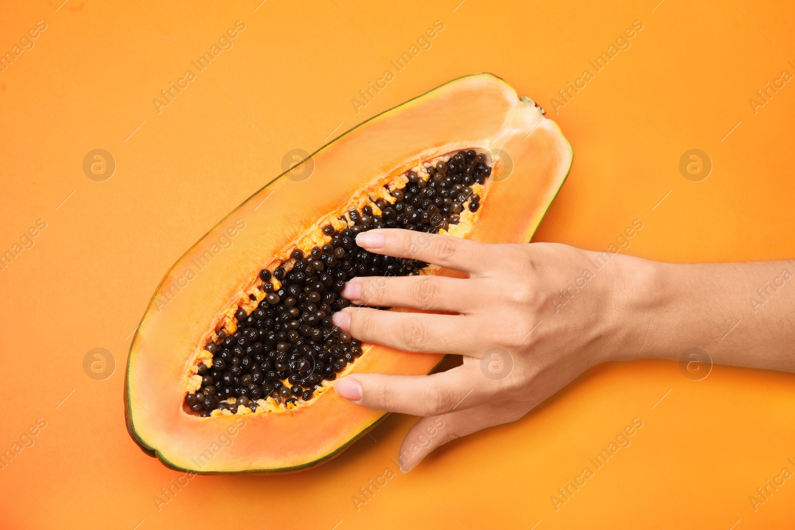 Photo of Young woman touching half of papaya on orange background, top view. Sex concept