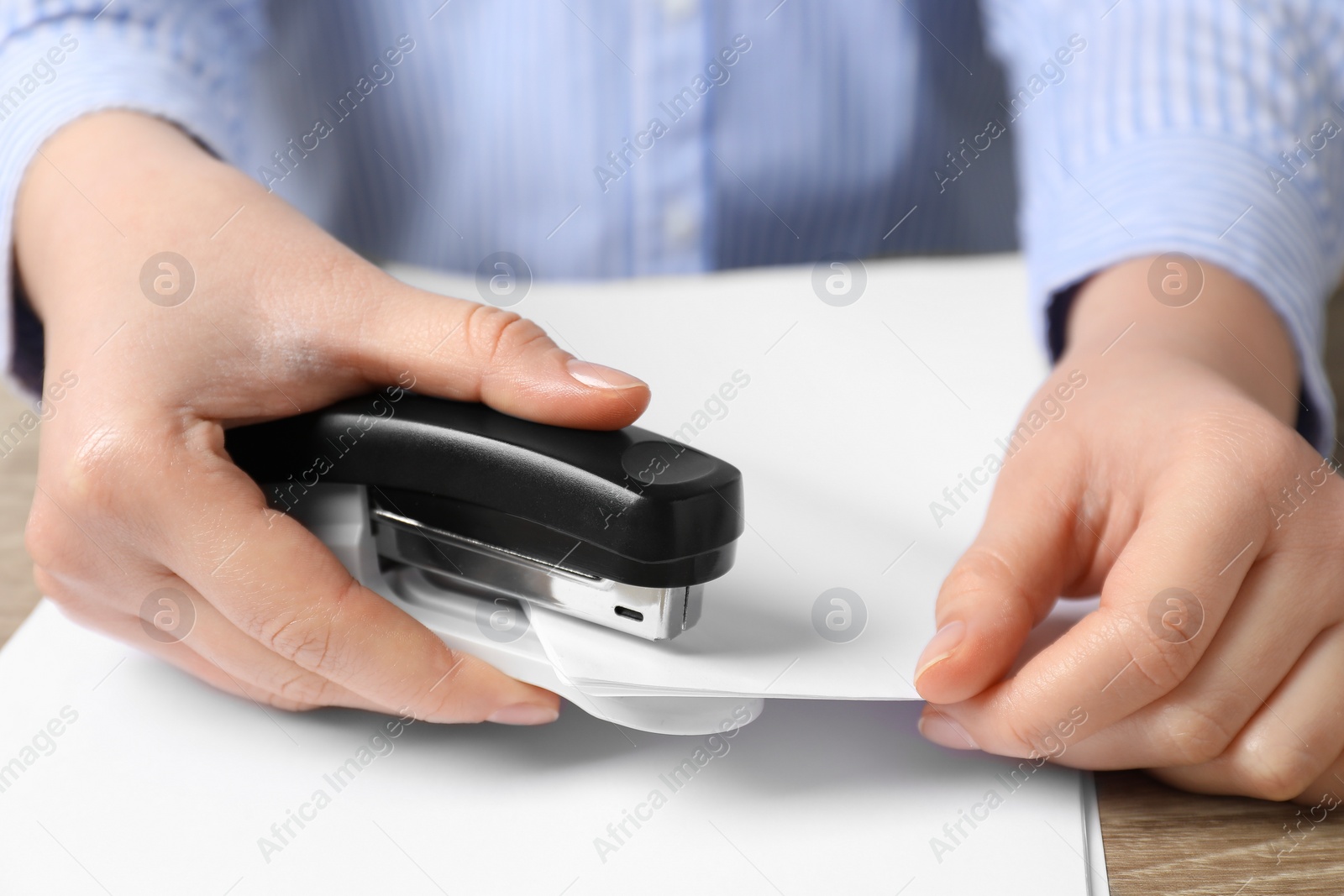 Photo of Woman with papers using stapler at table, closeup view