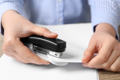 Photo of Woman with papers using stapler at table, closeup view