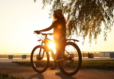 Young African-American woman with bicycle on city waterfront at sunset