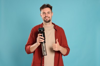 Photo of Smiling man holding sous vide cooker and showing thumb up on light blue background