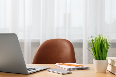 Home office. Laptop, smartphone, plant and stationery on wooden desk indoors. Space for text