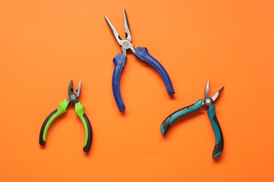 Different pliers on orange background, flat lay