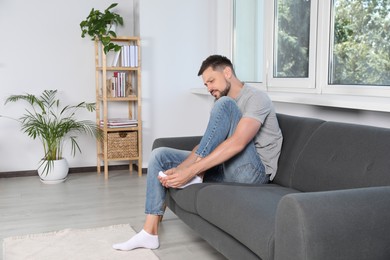 Photo of Man suffering from foot pain on sofa at home, space for text