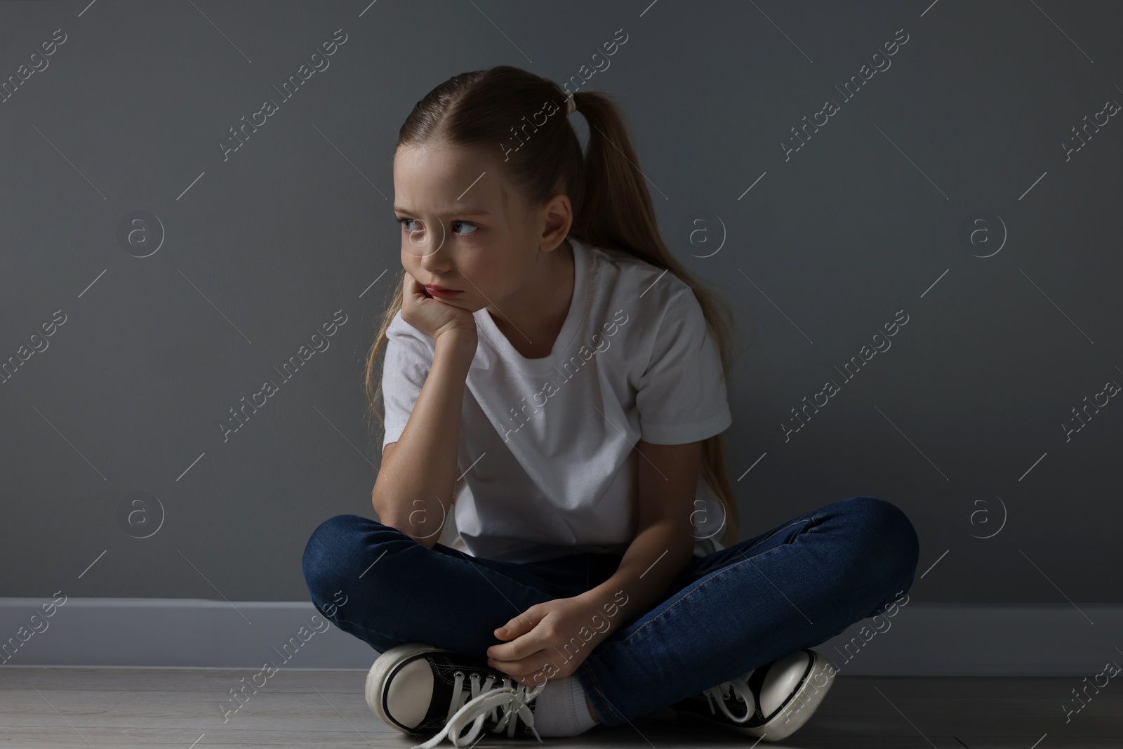 Photo of Sad girl sitting on floor near dark grey wall indoors