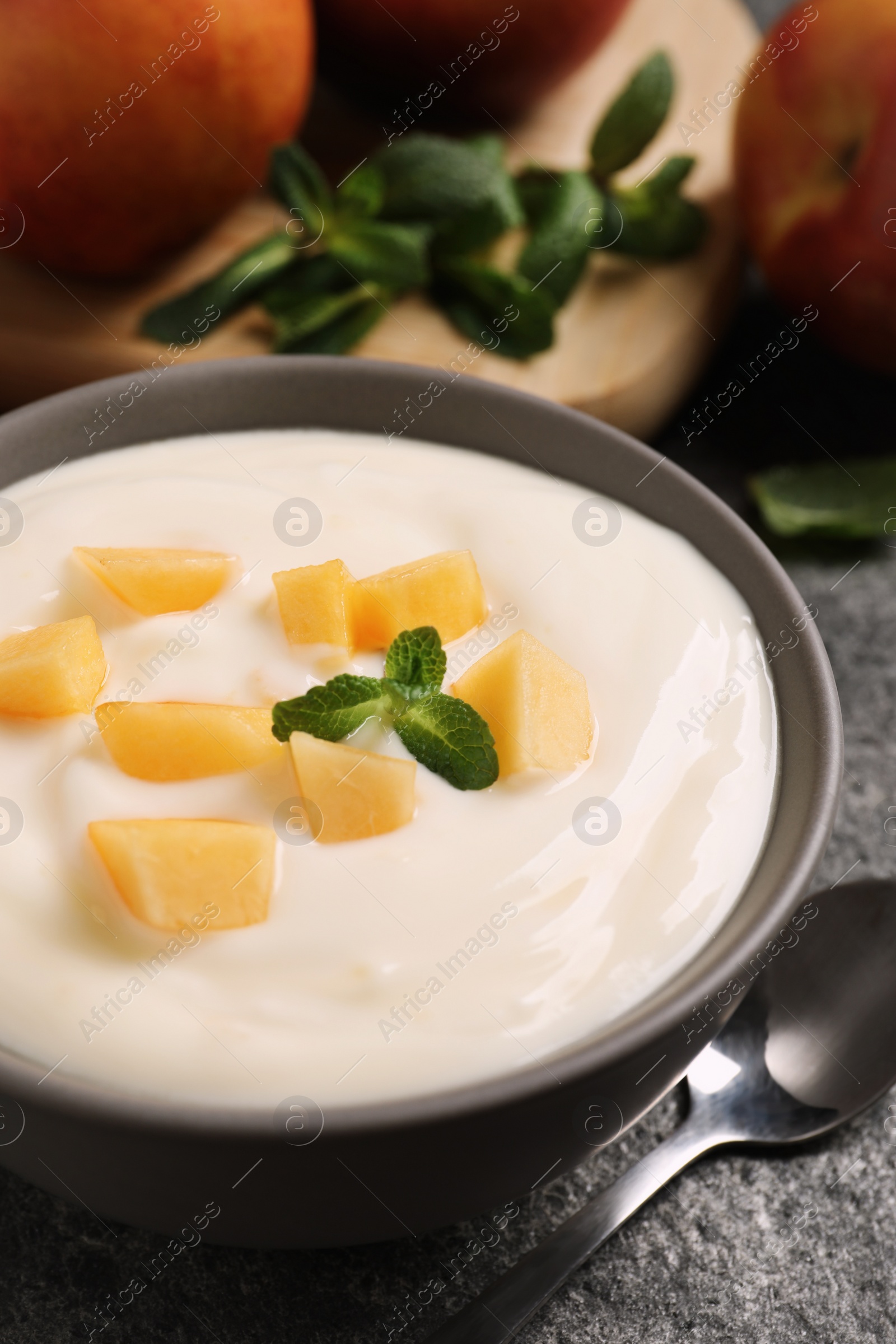 Photo of Delicious yogurt with fresh peach and mint on grey table, closeup