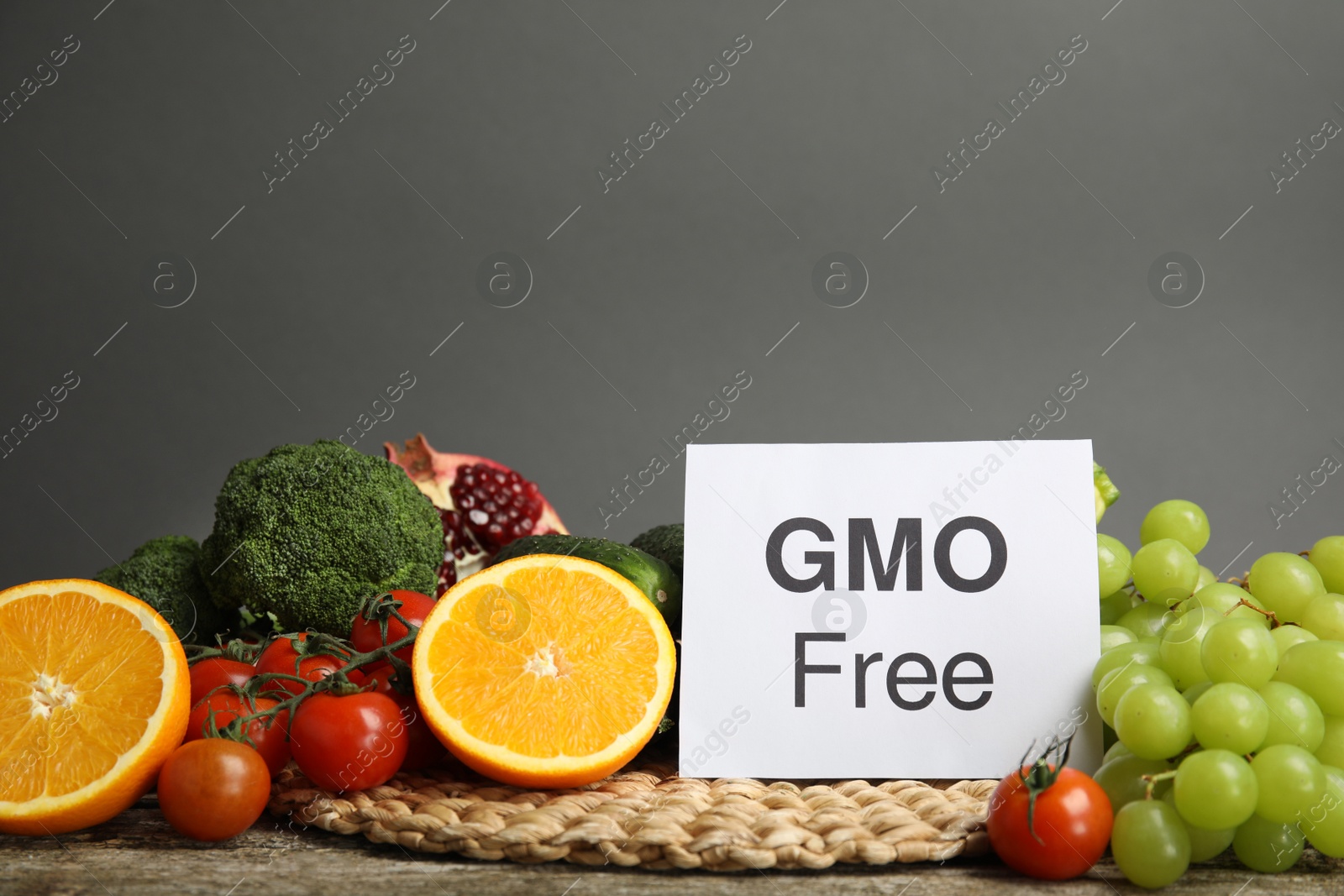 Photo of Tasty fresh GMO free products and paper card on wooden table against grey background