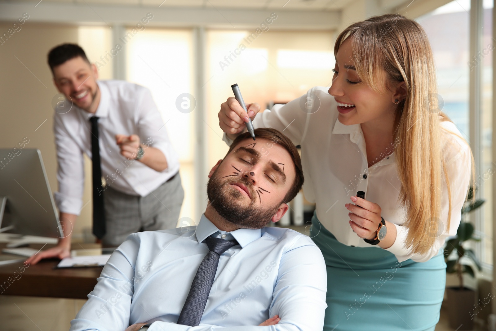 Photo of Young woman drawing on colleague's face while he sleeping in office. Funny joke