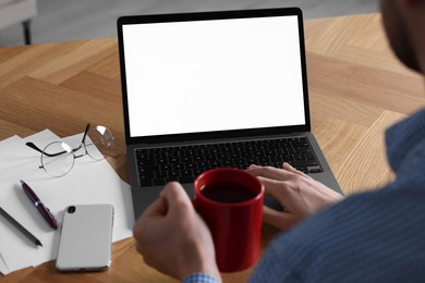 Photo of Man with cup of drink working on laptop at wooden desk, closeup