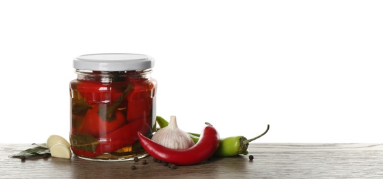 Photo of Glass jar of pickled chili peppers and ingredients on wooden table against white background. Space for text