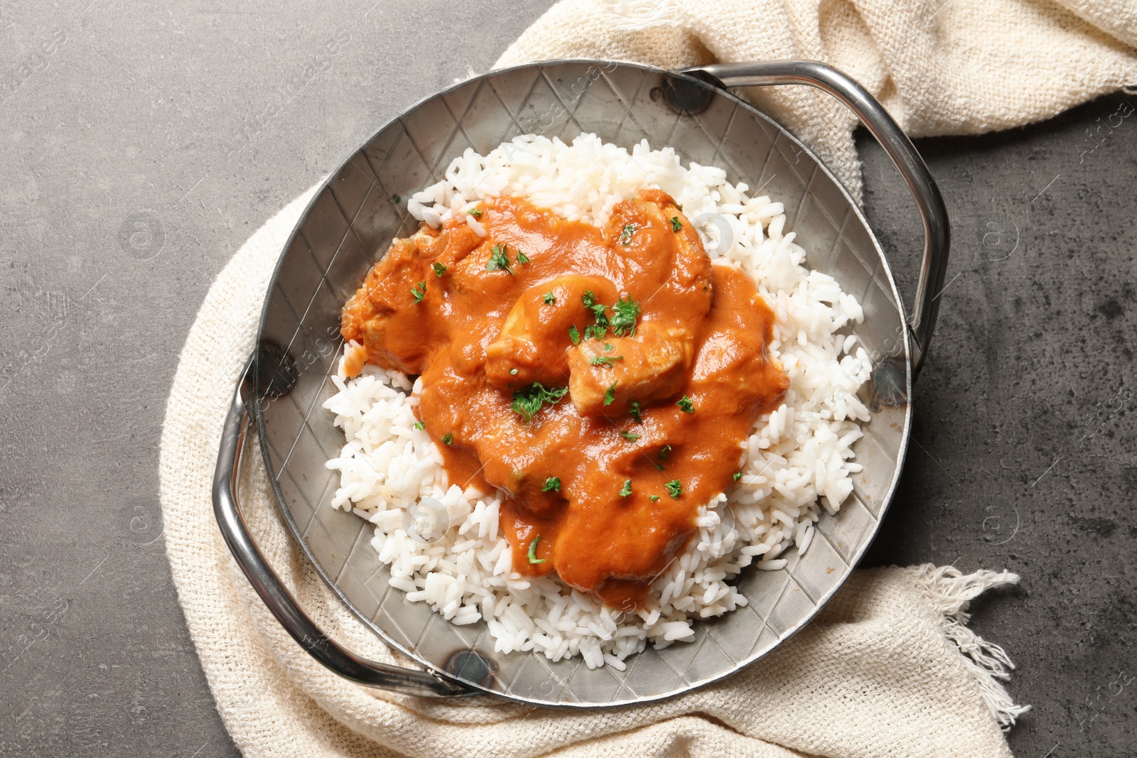 Photo of Delicious butter chicken with rice in dish and napkin on grey background, top view