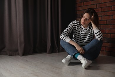 Photo of Sad young woman sitting on floor indoors, space for text