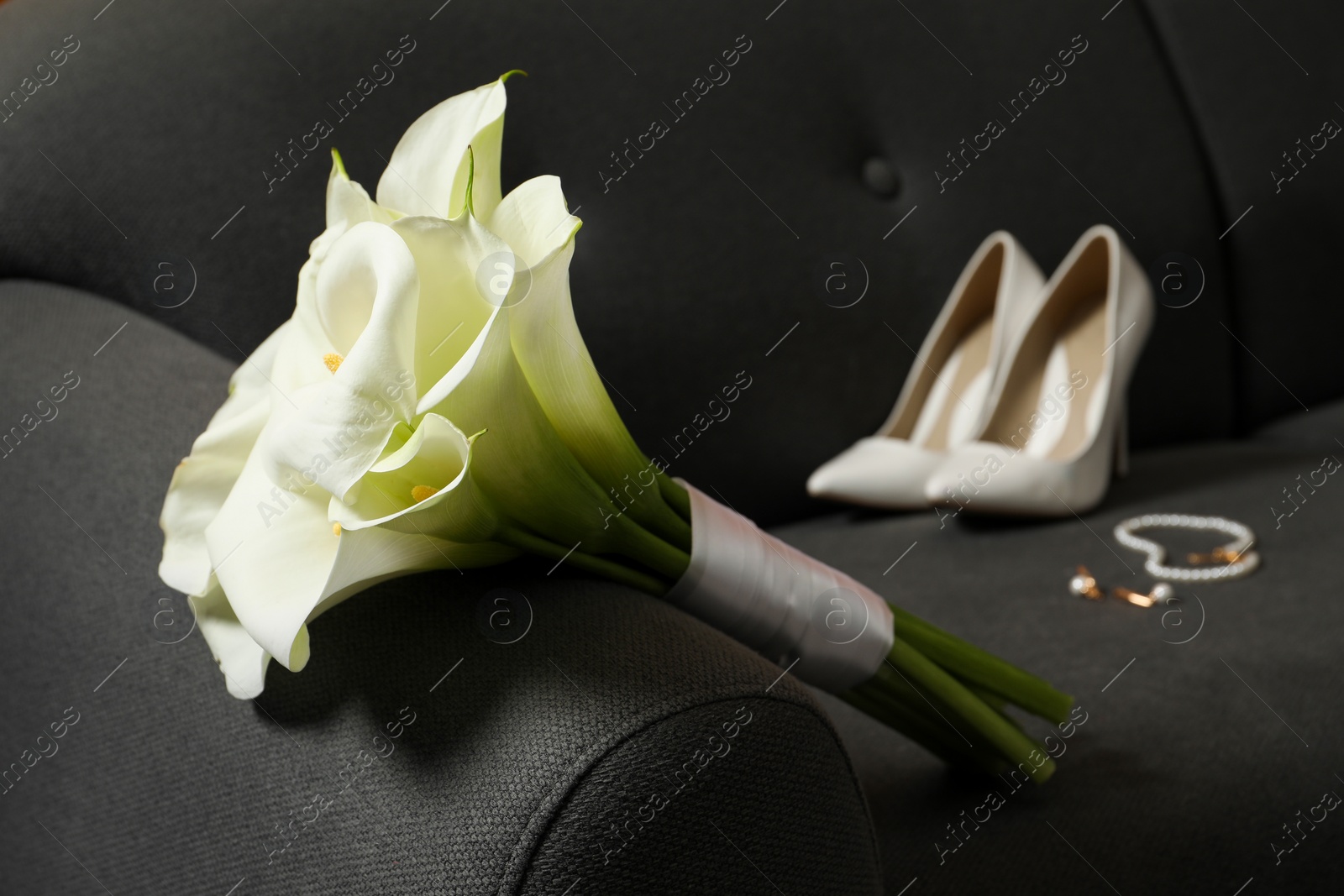 Photo of Beautiful calla lily flowers tied with ribbon, shoes and jewelry on sofa