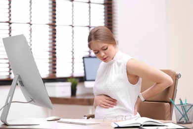 Photo of Young pregnant woman suffering from pain while working in office