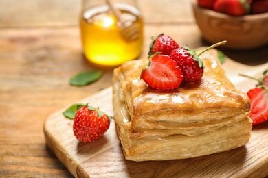 Fresh delicious puff pastry with sweet strawberries on wooden table, closeup. Space for text