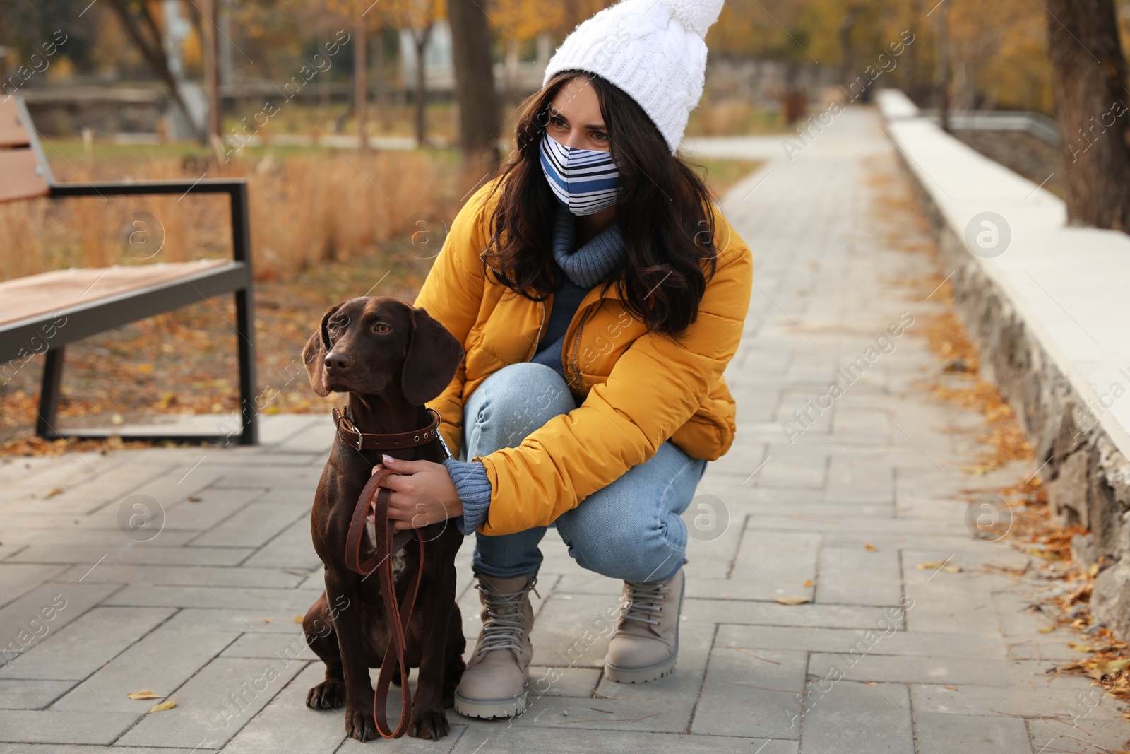 Photo of Woman in protective mask with German Shorthaired Pointer in park. Walking dog during COVID-19 pandemic