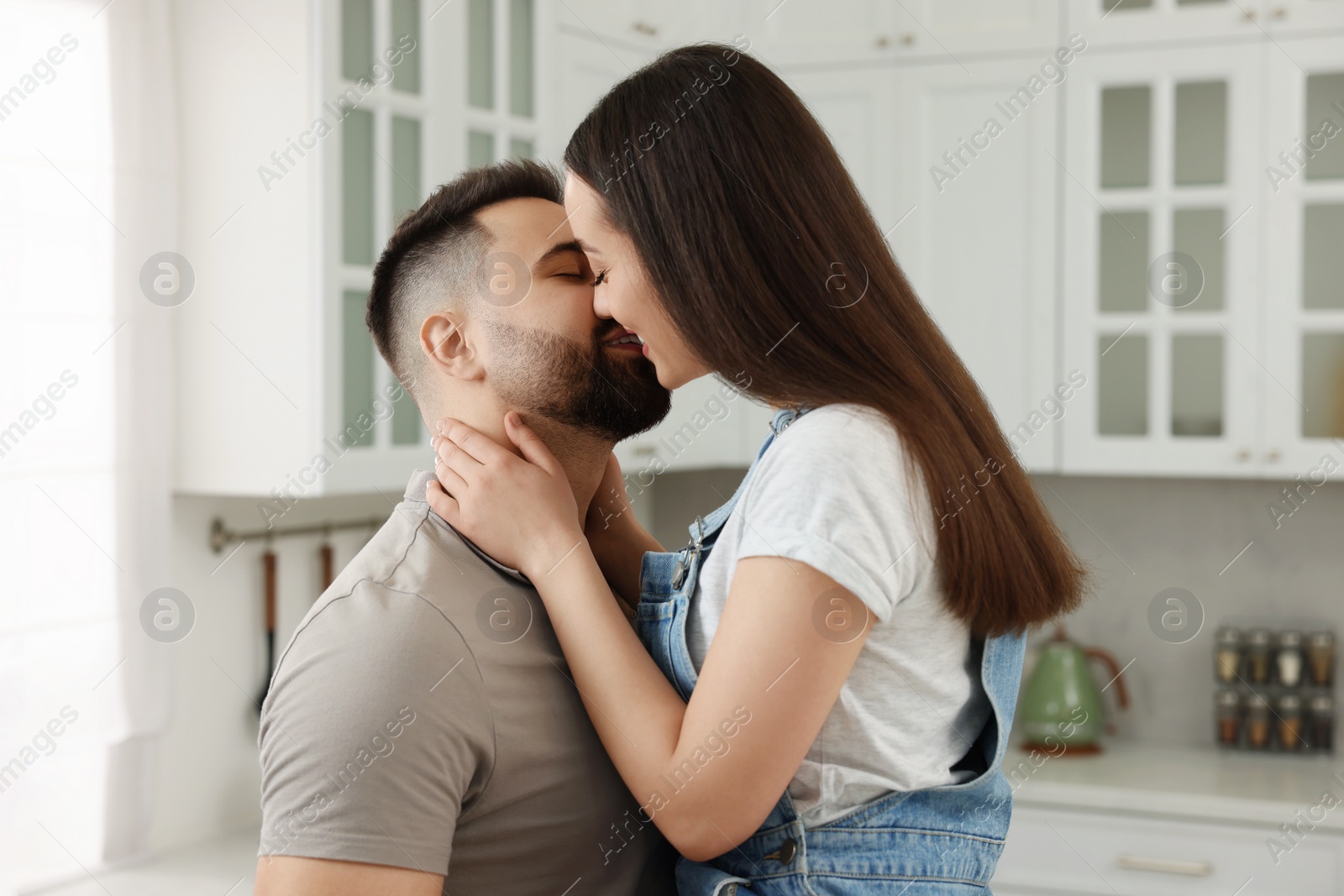 Photo of Affectionate young couple kissing in light kitchen