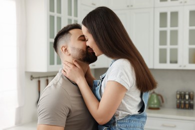 Photo of Affectionate young couple kissing in light kitchen