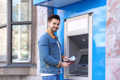 Photo of Young man with money near cash machine outdoors